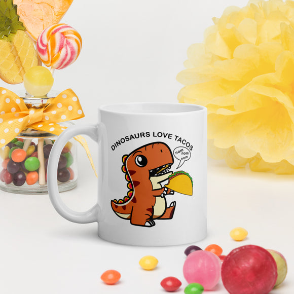 dinosaurs love tacos text over a cute dinosaur eating a taco saying nom nom nom in a text bubble on a glossy white ceramic mug 11 oz. and 15 oz.